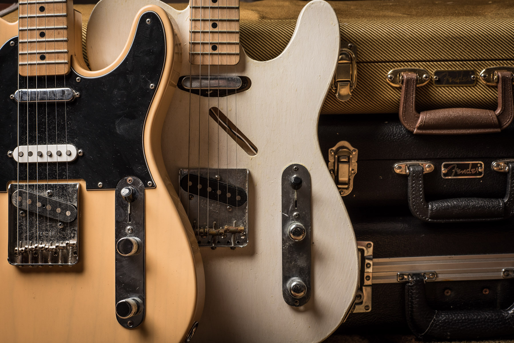 two fender telecasters in front of a stack of guitar cases.